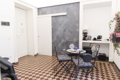 Camera Sovereign Herb presso il B&B I MORI Catania con zona pranzo, sedie in ferro battuto nero, angolo cottura e parete grigia accent