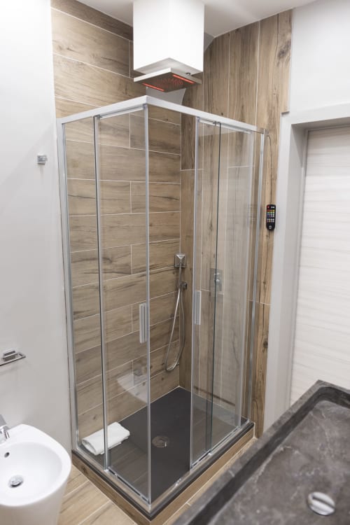 Moderno box doccia con rivestimento effetto legno e base nera nel bagno di B&B I MORI Catania