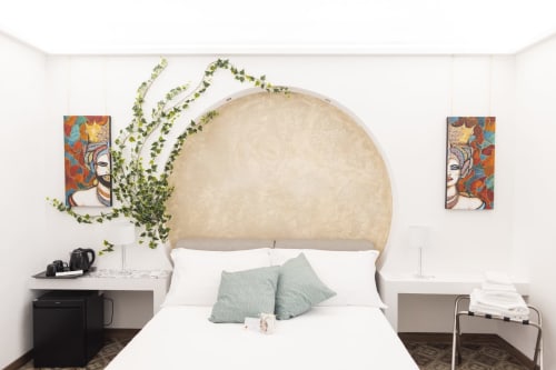 Quarto moderno do B&B I MORI Catania com grande cabeceira curva bege, cama branca, almofadas verdes e decoração de hera.