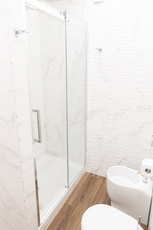 Banheiro moderno no B&B I MORI Catania com paredes de mármore, chuveiro integrado, piso de madeira e peças em branco