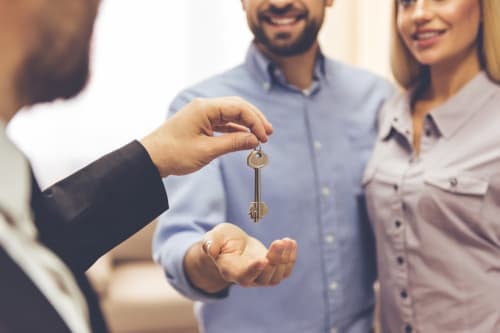 Agent immobilier remettant les clés de la maison à un jeune couple heureux à la Conciergerie Des Climats, Beaune