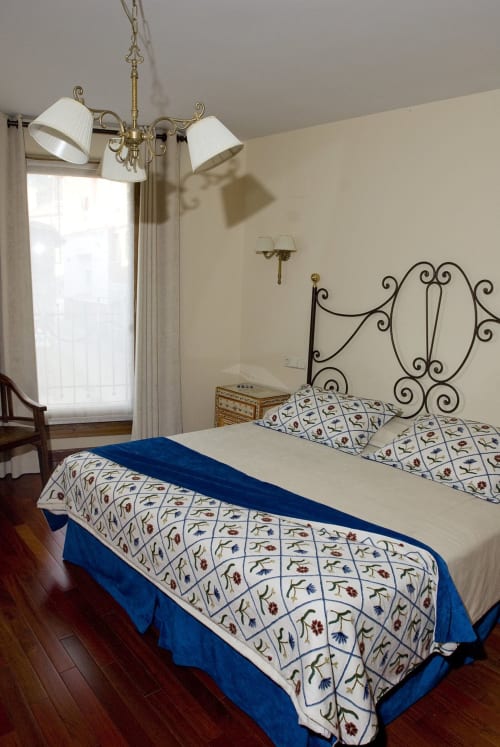 Elegante habitación en La Posada Del Tiétar con camas gemelas, cabecero de hierro ornamental y araña de latón con vistas a la montaña