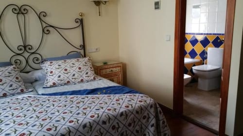 Dormitorio en La Posada Del Tietar con cama de hierro forjado, ropa de cama estampada y baño privado con azulejos azules y amarillos