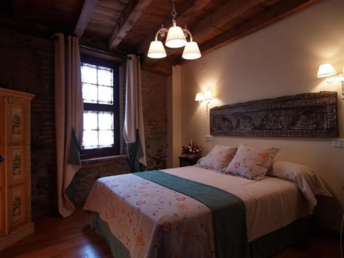 Dormitorio rústico en La Posada Del Tietar con vigas de madera, cama queen y ventana con vista a la ciudad