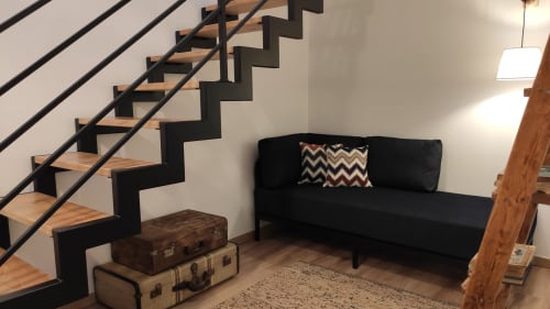 Escada moderna com degraus de madeira e estrutura preta ao lado de sofá preto no quarto Kindnessmoon Óbidos