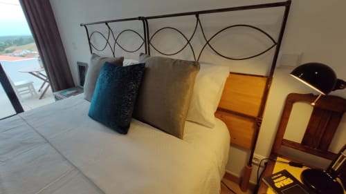 Quarto com cabeceira metálica decorativa, almofadas em camadas e vista para o mar na varanda de hotel em Óbidos, Portugal