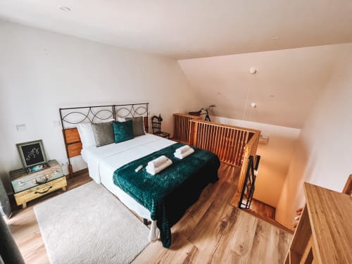 Quarto aconchegante em Kindnessmoon em Óbidos com cama de casal, roupa de cama verde-azulada, mesa-de-cabeceira em madeira e teto inclinado com claraboias
