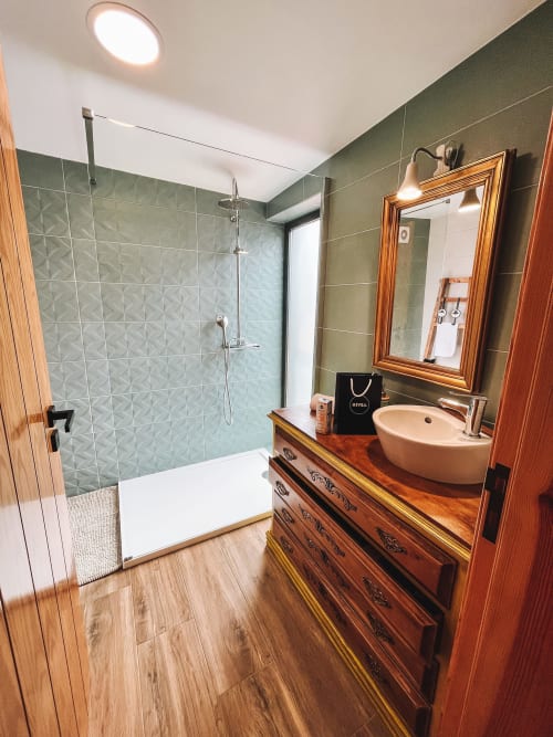 Banheiro moderno no Kindnessmoon em Óbidos com chuveiro em azulejos verdes, cuba de madeira, pia redonda e espelho aquecido