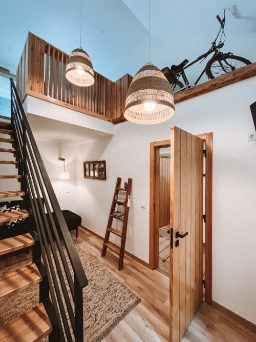 Entrada de loft moderno no Kindnessmoon em Óbidos com escadas de madeira, luminárias de palha tecida e decoração com bicicleta