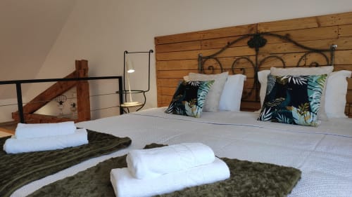 Quarto aconchegante na Kindnessmoon Óbidos com cabeceira de madeira, almofadas tropicais, roupa de cama branca e toalhas dobradas na cama.