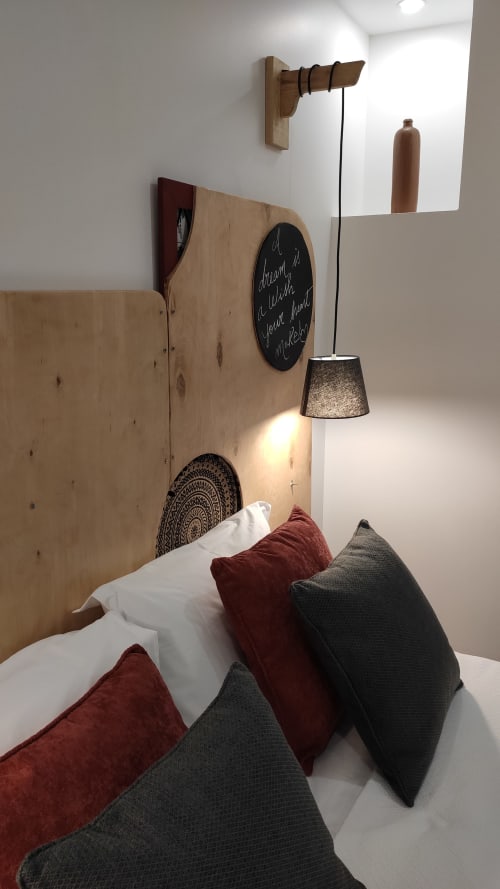 Quarto aconchegante na Kindnessmoon em Óbidos com cabeceira de madeira, luminária pendente, almofadas bordô e cinza, e parede com lousa
