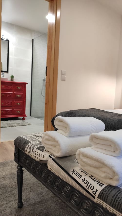 Quarto da Kindnessmoon em Óbidos com toalhas brancas frescas, cama com estrutura escura, cômoda vermelha e casa de banho privativa