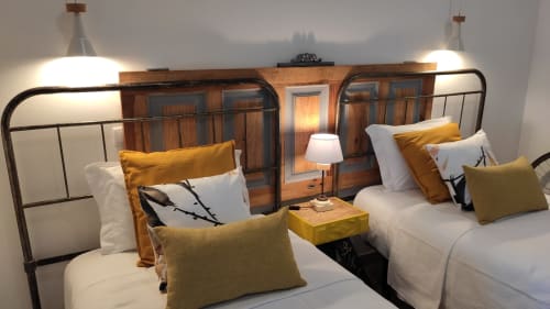 Quarto duplo da Kindnessmoon em Óbidos com camas de ferro, roupa de cama branca, almofadas douradas, móveis de madeira e iluminação pendente