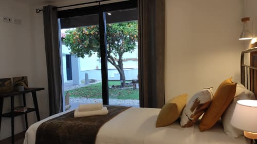 Quarto moderno na Kindnessmoon em Óbidos com vista para o jardim, cama com almofadas douradas e portas de vidro que abrem para o terraço