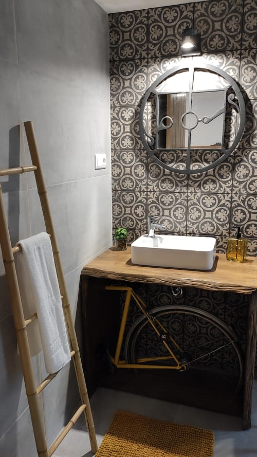 Banheiro moderno no Kindnessmoon Óbidos com azulejos ornamentados, espelho redondo, pia em madeira e guarda-bicicletas vintage