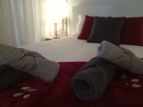 Quarto moderno em villa de Óbidos com toalhas enroladas na cama, tapete vermelho, almofadas decorativas e vista da cidade pela janela