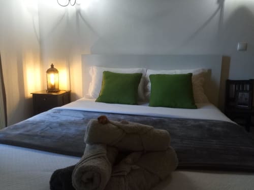 Quarto na Kindnessmoon em Óbidos com cama branca, almofadas verdes, iluminação aconchegante e toalhas enroladas