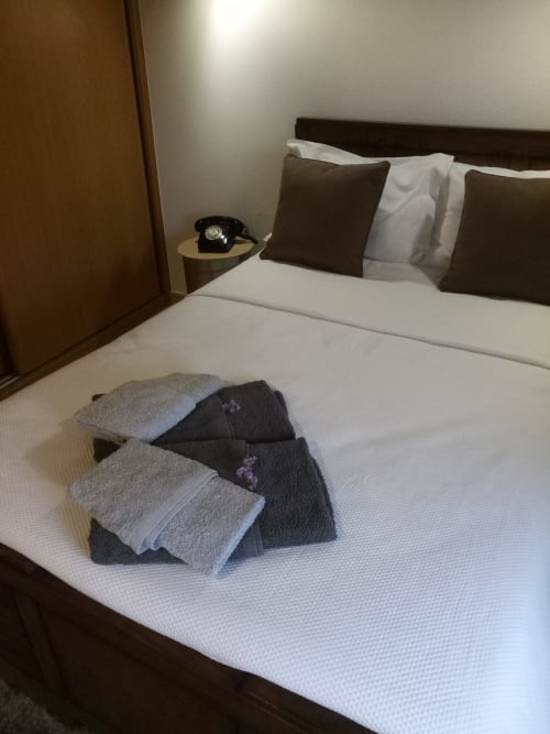 Toalhas arrumadas na cama da vila Kindnessmoon em Óbidos, Portugal, com criado-mudo e telefone rotativo preto