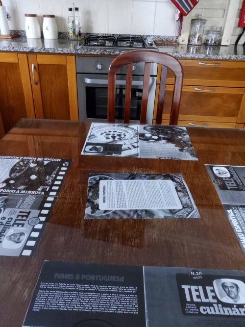 Mesa de jantar na cozinha de villa portuguesa com revistas gastronômicas, livros de receitas, móveis de madeira e granito