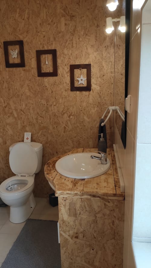 Banheiro rústico com paredes de cortiça, vaso sanitário branco, pia redonda em bancada de madeira, molduras decorativas e espelho na Casa