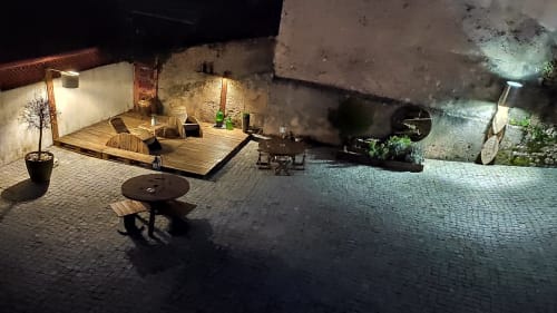 Pátio noturno da Casa d'Amélia em Óbidos com áreas iluminadas, deck de madeira, churrasqueira e paredes de pedra rústica