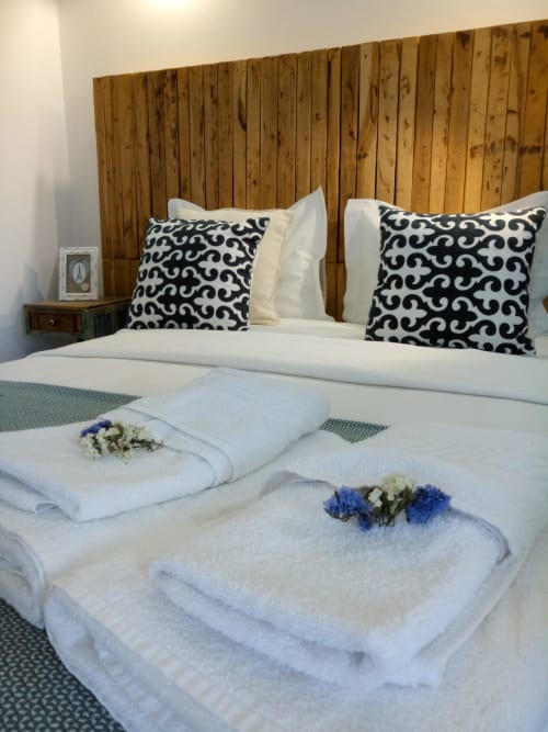 Quarto com cabeceira em madeira, roupa de cama branca, almofadas estampadas em preto e toalhas enroladas com flores na Casa d'Amélia, Óbidos