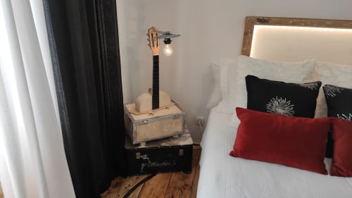 Canto do quarto com guitarra acústica em mala, almofadas vermelhas na cama e vista para a cidade na villa de Óbidos
