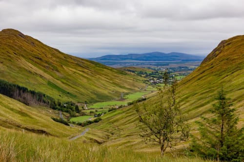 Scenic valley view from Donegal mountains with green hills, winding river, and distant village nestled in lush Irish