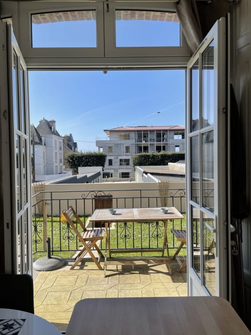 Portes du balcon ouvertes au Roc Fleuri Saint Malo, vue sur le jardin, mobilier en bois et ciel bleu dégagé