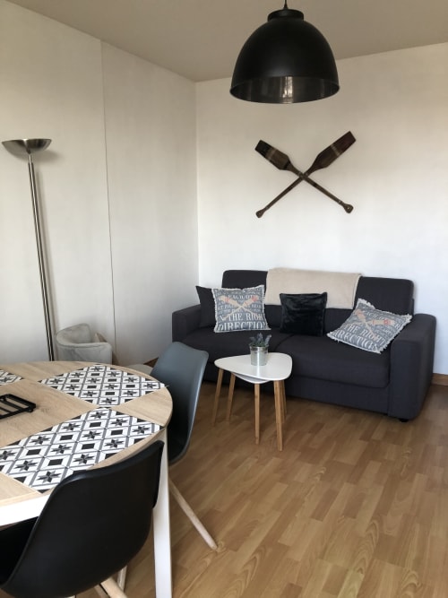 Séjour moderne à la Résidence Le Roc Fleuri à Saint-Malo avec canapé noir, table à manger et luminaires suspendus