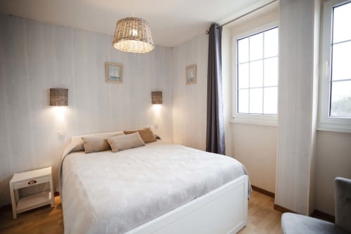 Chambre lumineuse à la Résidence Le Roc Fleuri à Saint Malo avec lit blanc, luminaire suspendu en rotin, vue mer et design moderne