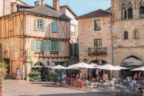 Place médiévale de Figeac avec terrasse de café, bâtiments historiques en pierre et architecture colombagée