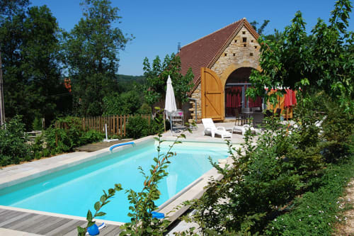 Chambres d'hôtes Les Pratges à Figeac : maison en pierre avec piscine turquoise, transats et jardins luxuriants sous ciel bleu.