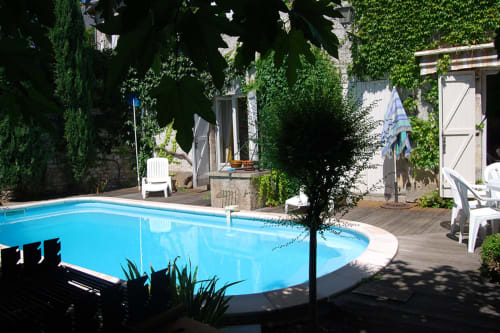 Piscine bleue entourée de murs couverts de lierre et terrasse en bois aux Chambres d'hôtes Les Pratges, Figeac