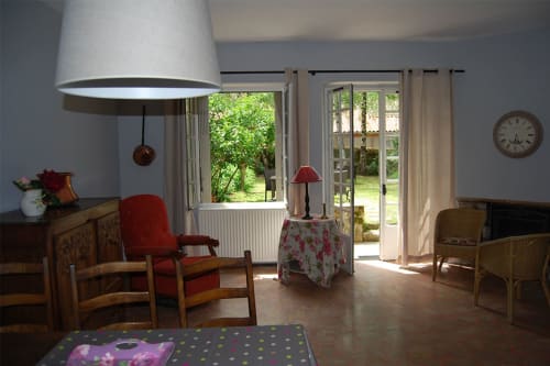 Séjour lumineux aux Pratges B&B à Figeac avec fauteuil rouge, lampe suspendue et vue sur le jardin