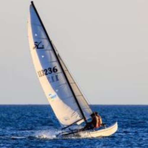 Barca a vela con vele blu e bianche nel mare blu profondo vicino a Torre Grande Oristano