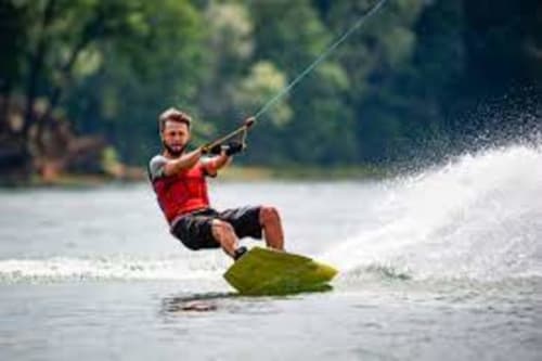 Uomo che pratica wakeboard sull'acqua vicino a Torre Grande Oristano con sfondo di foresta