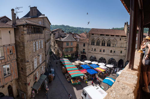 Place médiévale de Figeac avec des étals de marché colorés et des bâtiments historiques en pierre