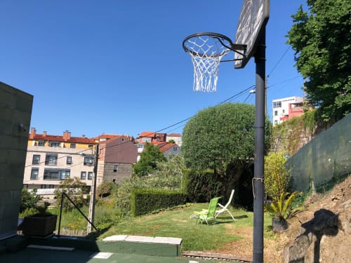 Canasta de baloncesto en el jardín de Casa Arealonga en Vigo, España, con silla verde y edificios de la ciudad
