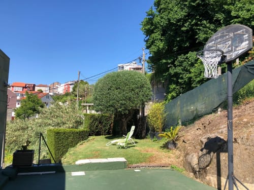 Zona de recreo en el jardín de Casa Arealonga en Vigo con canasta de baloncesto, césped y vistas a la ciudad