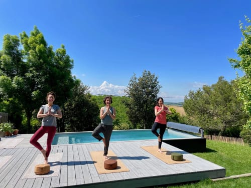 Three women practicing yoga by infinity pool at Maison Monsieur Léger with countryside views in Montaut