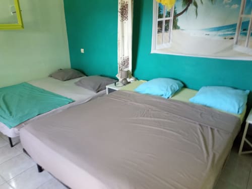 Chambre turquoise éclatante à la maison d'hôtes Caribgites à Sainte-Anne avec plusieurs lits et affiche vue sur plage