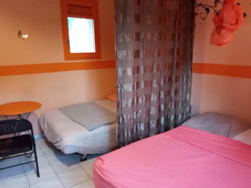 Chambre double colorée du gîte Caribgites à Sainte-Anne avec lits rose et blanc, murs orange et vue jardin