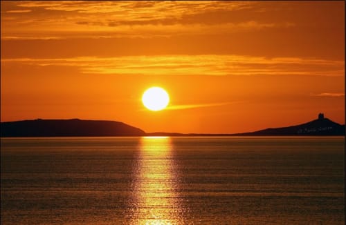 Tramonto dorato sul mare a Torre Grande Oristano, con riflessi dorati sulle acque tranquille e isole silhouettate