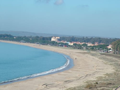 Vista panoramica della spiaggia di Torre Grande Oristano con acque turchesi, spiaggia sabbiosa e edifici costieri