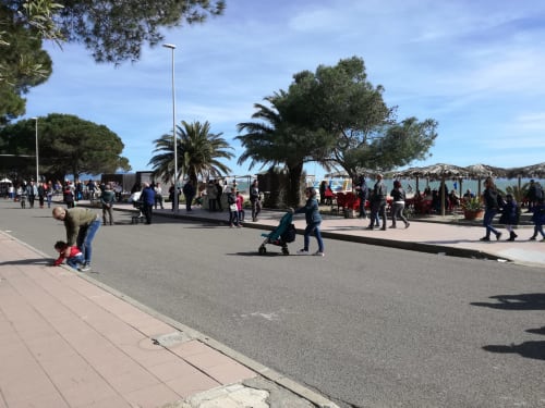 Passeggiata sul lungomare a Torre Grande Oristano con famiglie che godono di una bella giornata soleggiata tra palme e il mare Mediterraneo