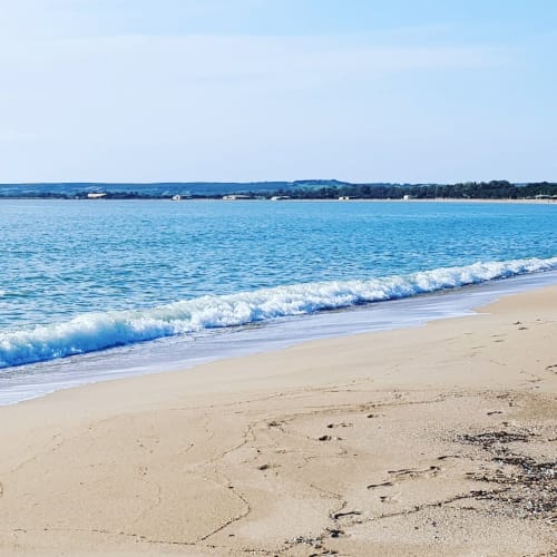 Spiaggia sabbiosa con onde increspate e villaggio costiero in lontananza a Torre Grande, Oristano