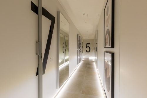 Corridoio moderno presso CASA LOUNGE ISTRIA a Cagliari con pavimento illuminato, porte numerate e opere d'arte contemporanea alle pareti