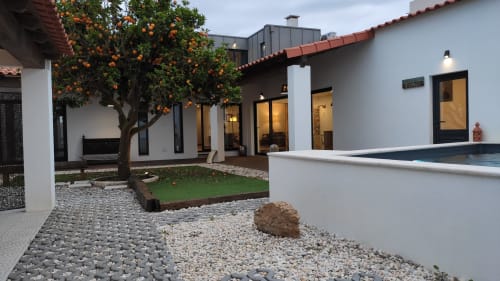Modern cottage courtyard in Óbidos with orange tree, white walls, black-framed windows, pool edge, and gravel patio