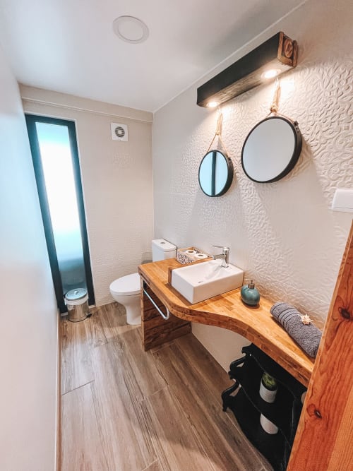 Modern bathroom with wooden vessel sink, round mirrors, and textured white walls in Kindnessmoon cottage, Obidos Portugal